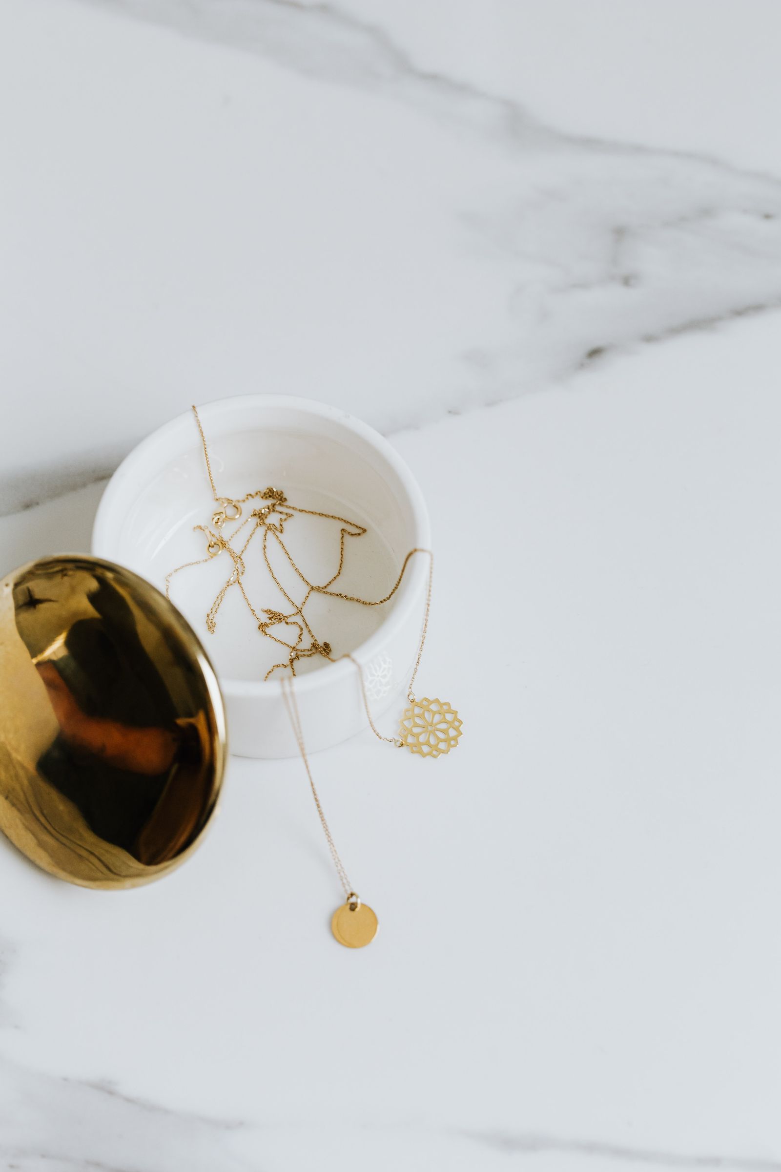 Fine gold chains stored in a small ceramic dish on marble