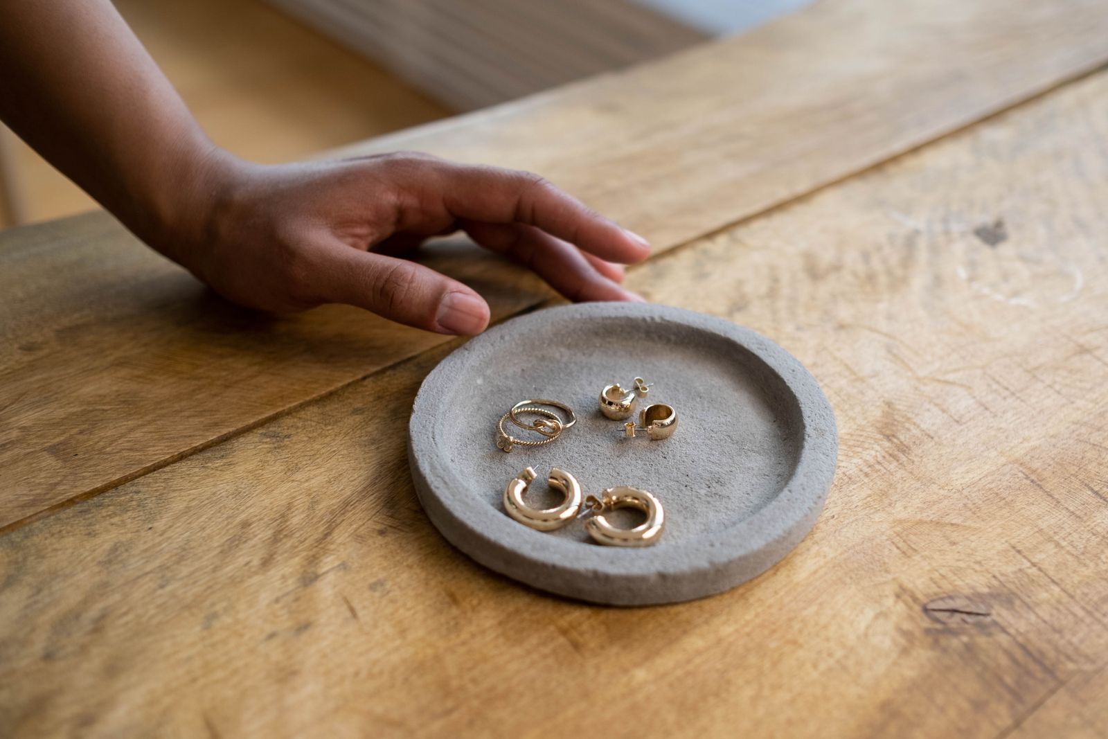 Gold hoop earrings and a ring resting in a stone jewellery dish