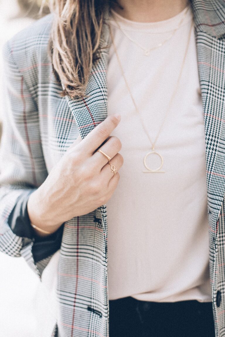Layered minimal gold necklaces and thin stacking rings worn with a blazer