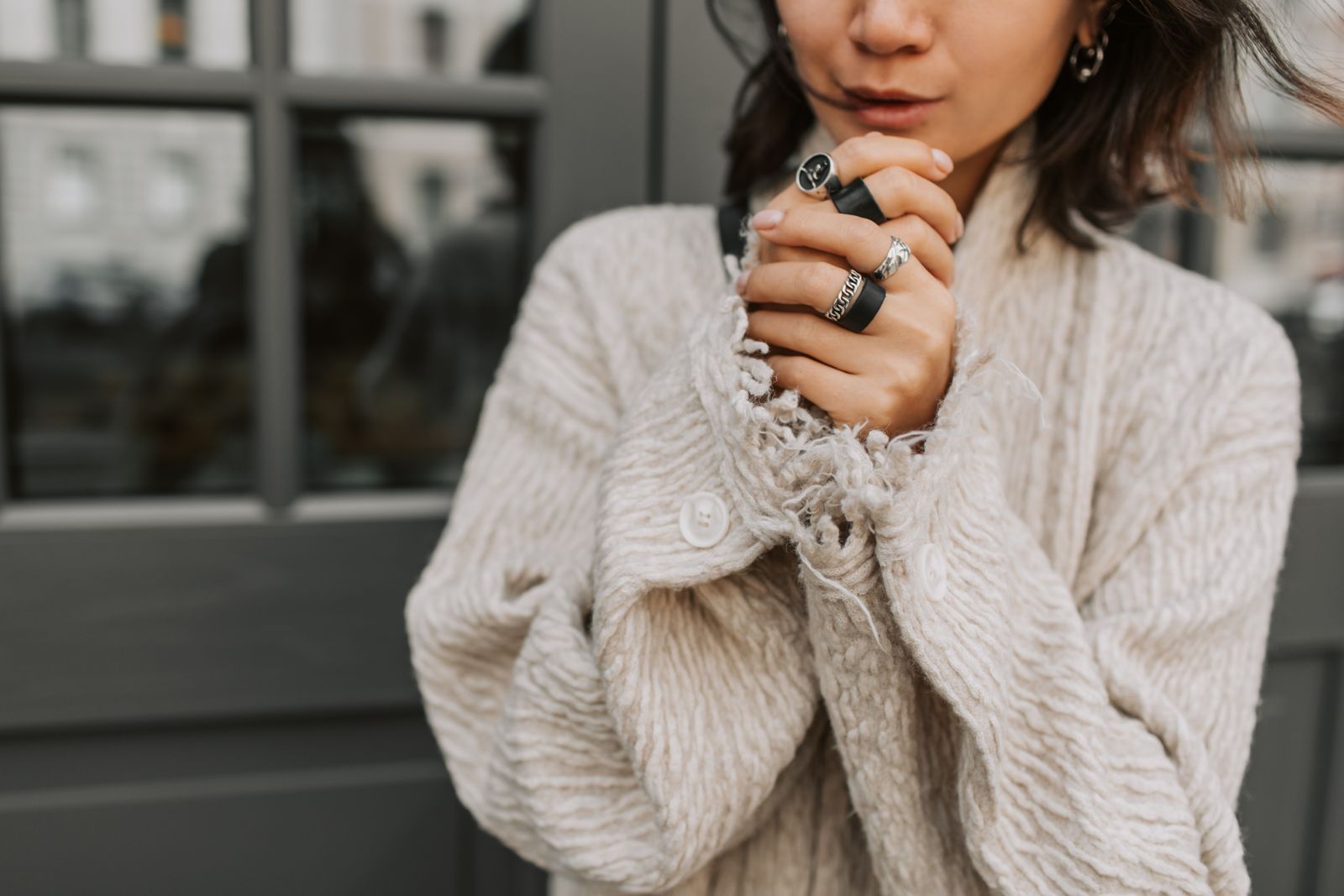 Stacked silver rings worn on both hands with a knitted coat