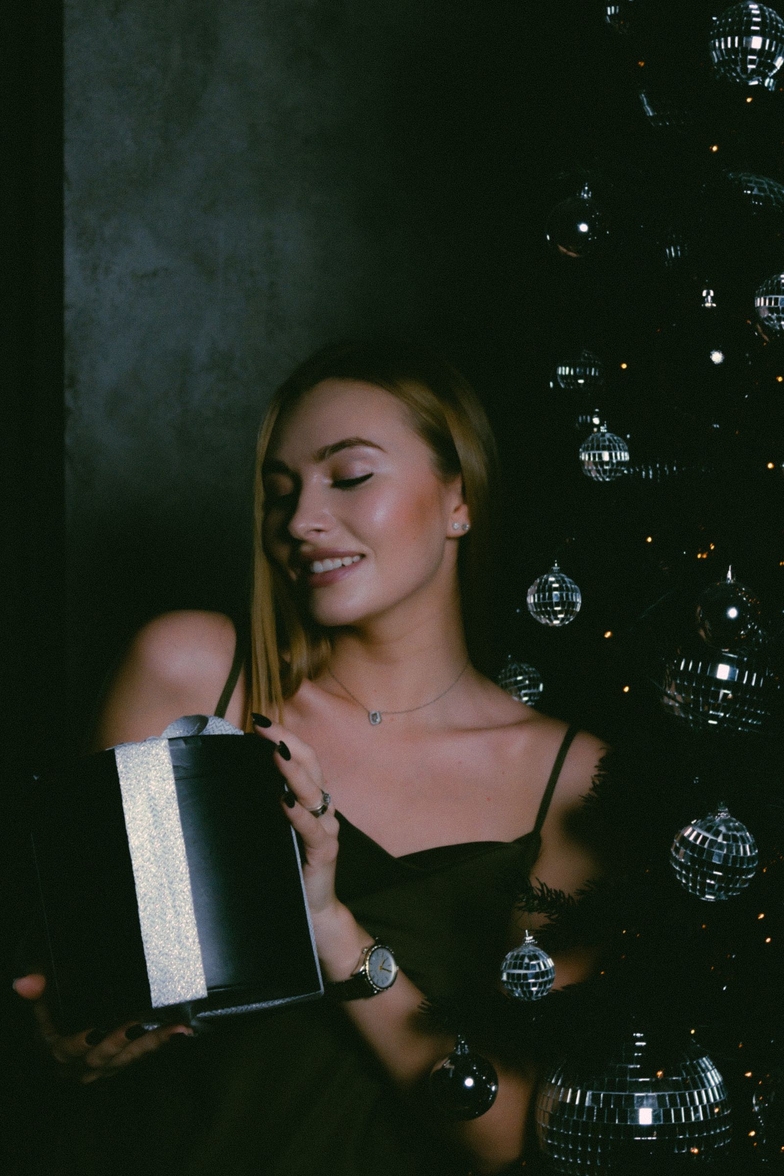 Woman in a party dress wearing a delicate necklace beside a Christmas tree